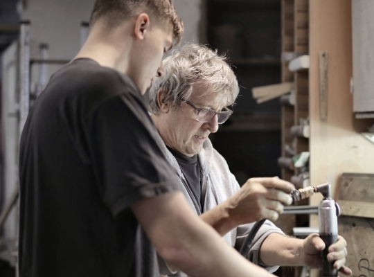 Man showing younger man what he's doing in a workshop environment