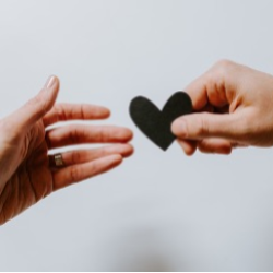 A hand holding a black cut out of a heart passing it to another hand